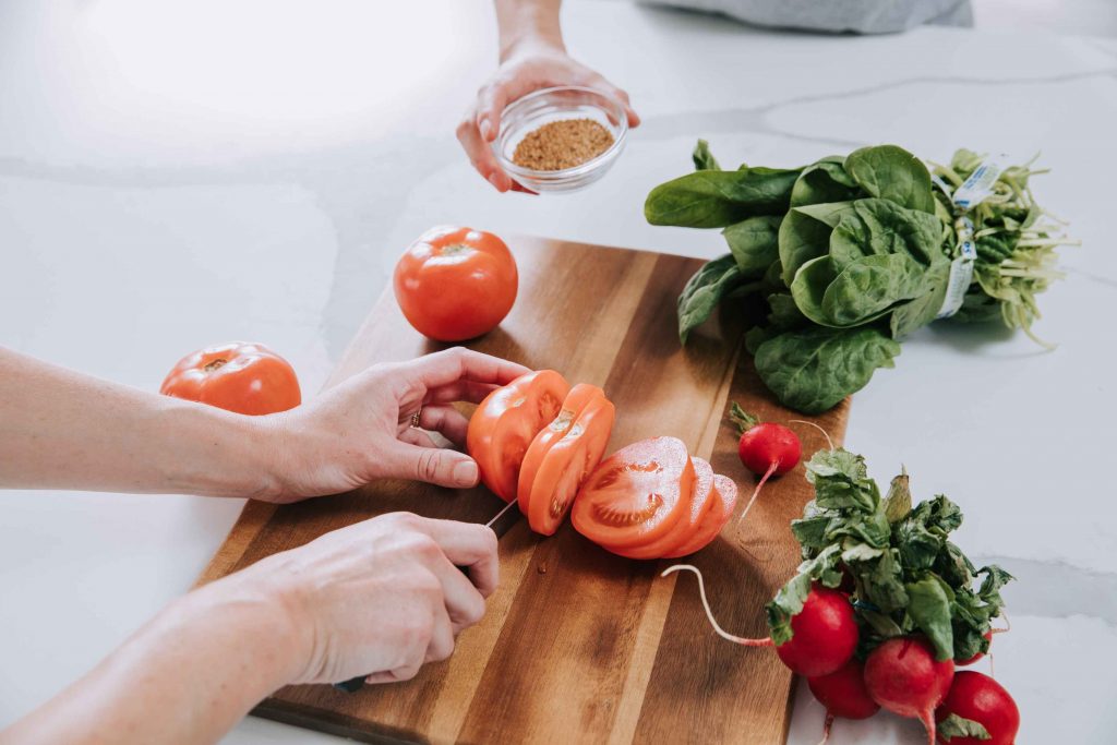 Slicing a tomato during meal prep. Tomatoes are a source of lycopene, a powerful antioxidant found in Nutrilite™ Double X™ multivitamin.