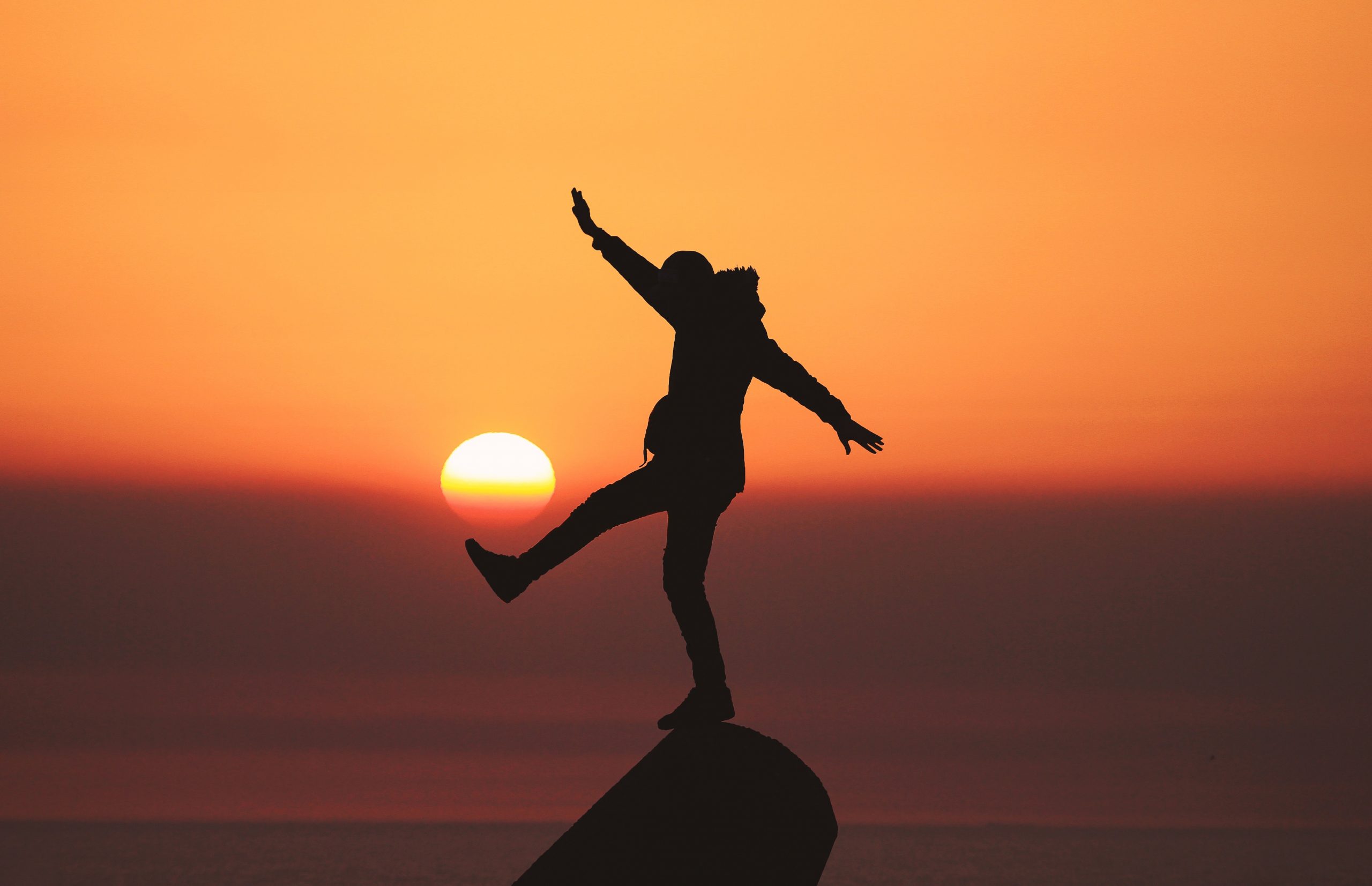A person balances atop a rock on one foot as the sun sets on the horizon. Staying energized and inspired to achieve your goals is easier when you live your life in balance.