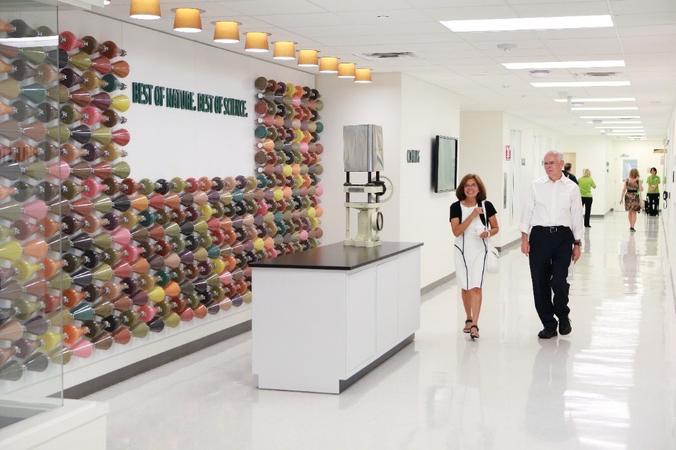 Two distributors walk past a wall that displays our Best of Nature, Best of Science motto. Flasks on the wall denote the colorful phytonutrient concentrates found within Nutrilite supplements.