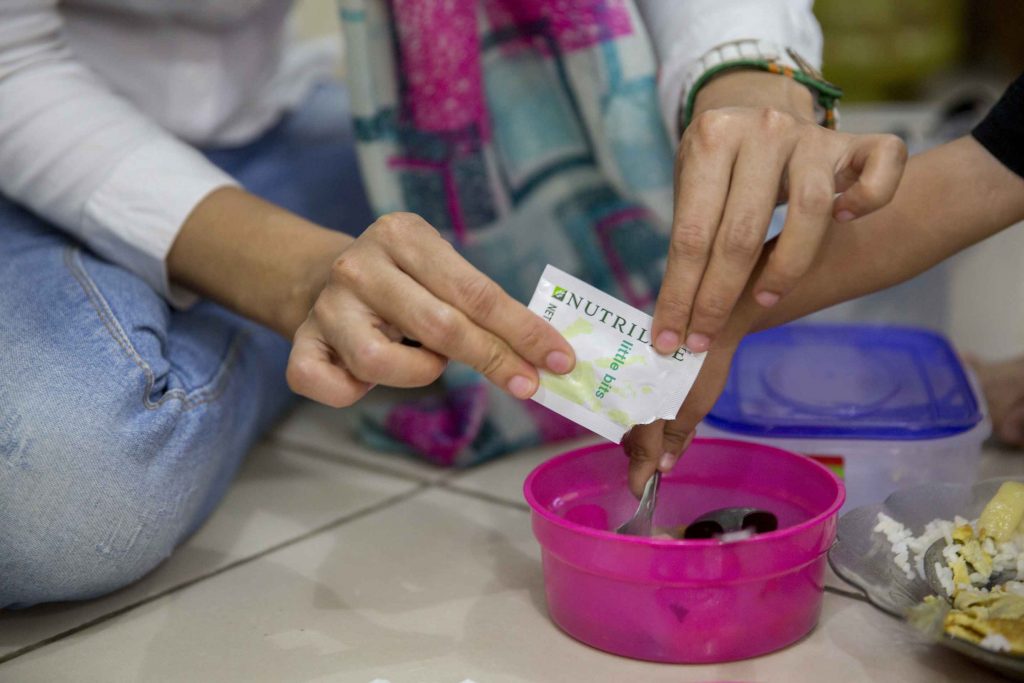 Caregiver adding Nutrilite Little Bits powder to a child’s meal. It’s as easy as adding contents of one sachet into food.