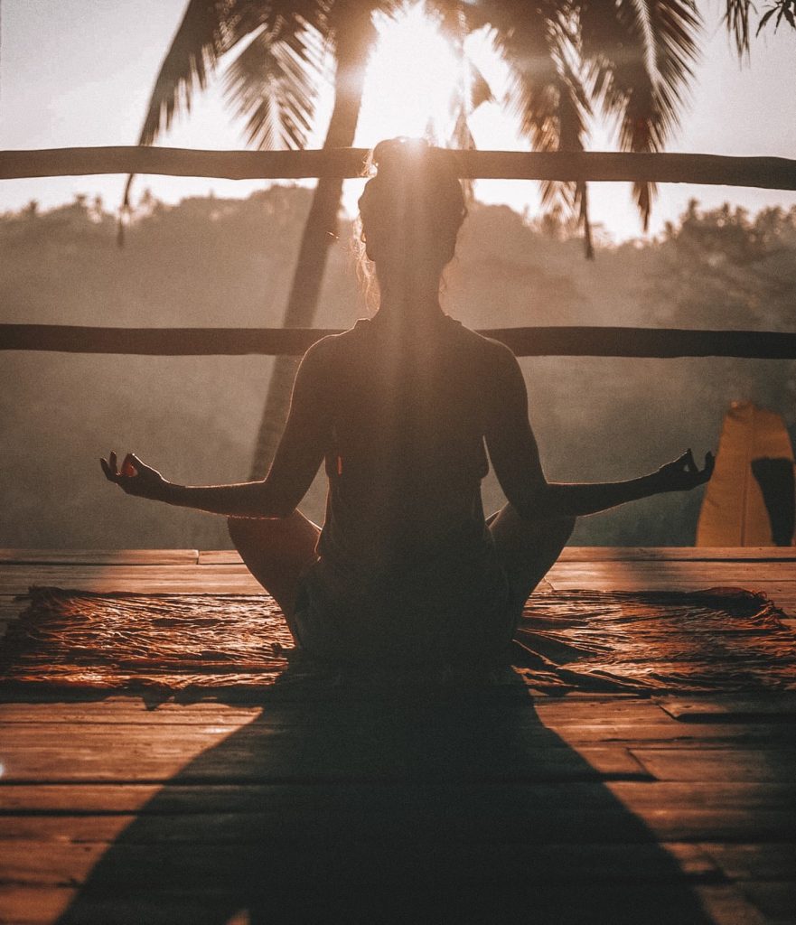 A woman practices yoga as the sun sets. Stress management and resilience has been identified as one of the ten domains of wellness.