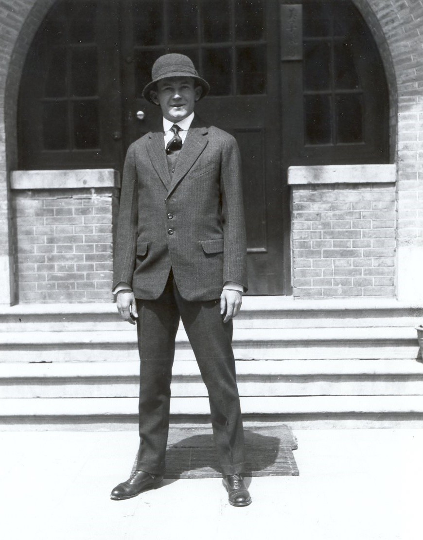 Historical image of man standing in front of steps leading up to a building facade.